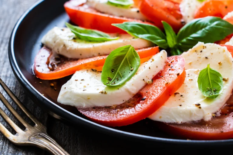Close up of a caprese salad with mozzarella cheese, tomatoes, and basil on a black plate.