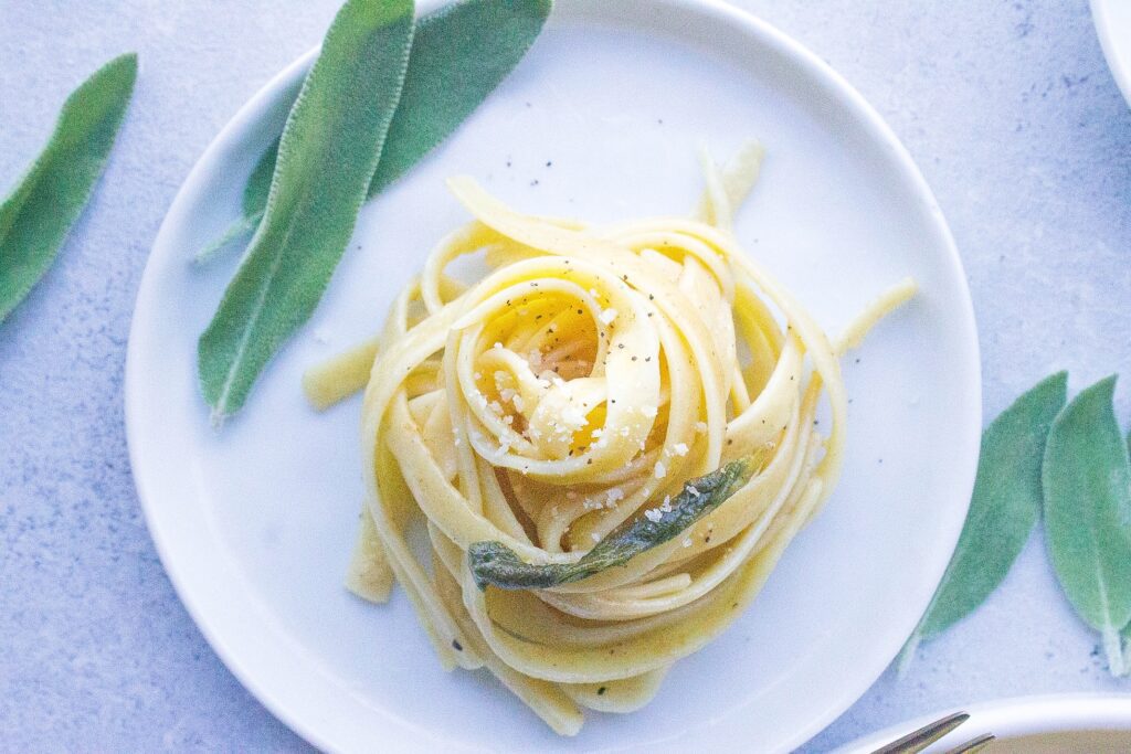 Fettuccine pasta coiled up with fresh sage decorating the plate and table